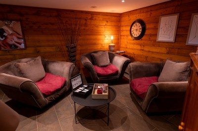 Chambre chaleureuse avec lits, canapé, fauteuils en osier, table basse et éclairage tamisé, décor rustique.