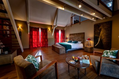 Chambre chaleureuse avec lits, canapé, fauteuils en osier, table basse et éclairage tamisé, décor rustique.