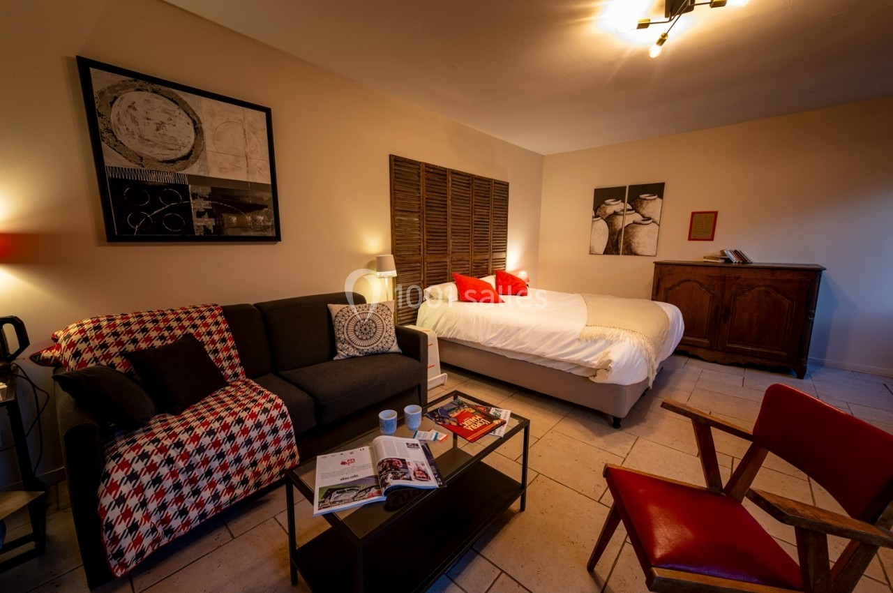 Chambre chaleureuse avec lit double, canapé, table basse, fauteuils, et décoration murale dans un style cosy.