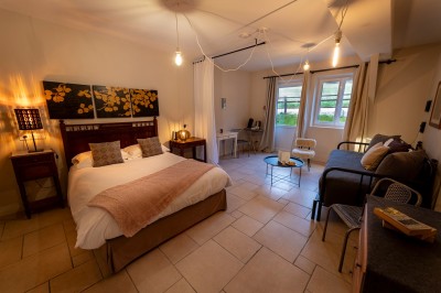 Chambre chaleureuse avec lits, canapé, fauteuils en osier, table basse et éclairage tamisé, décor rustique.