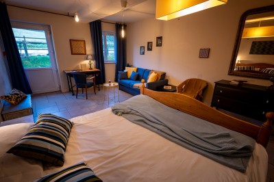 Chambre chaleureuse avec lits, canapé, fauteuils en osier, table basse et éclairage tamisé, décor rustique.