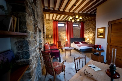 Chambre chaleureuse avec lits, canapé, fauteuils en osier, table basse et éclairage tamisé, décor rustique.