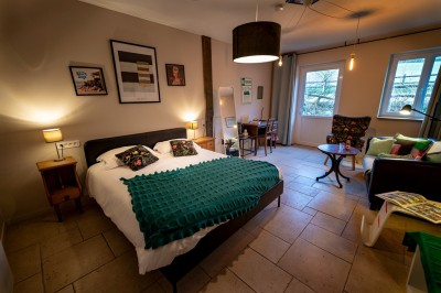 Chambre chaleureuse avec lits, canapé, fauteuils en osier, table basse et éclairage tamisé, décor rustique.