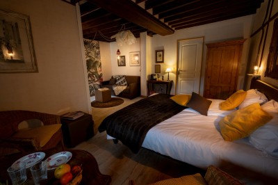 Chambre chaleureuse avec lits, canapé, fauteuils en osier, table basse et éclairage tamisé, décor rustique.