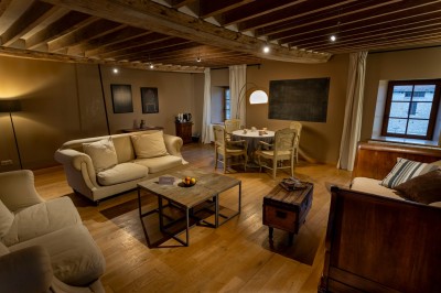 Chambre chaleureuse avec lits, canapé, fauteuils en osier, table basse et éclairage tamisé, décor rustique.