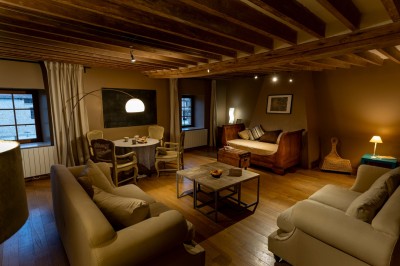 Chambre chaleureuse avec lits, canapé, fauteuils en osier, table basse et éclairage tamisé, décor rustique.