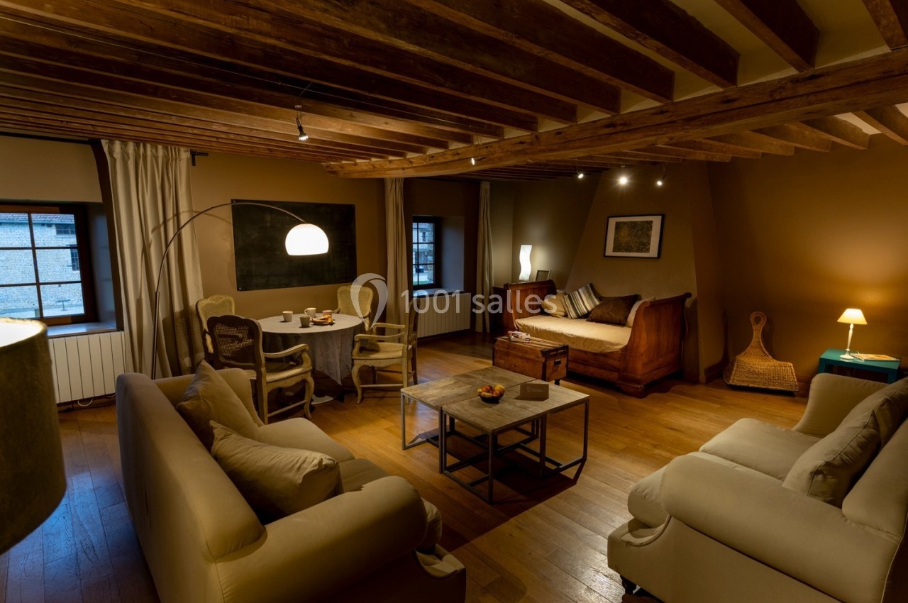 Salon chaleureux avec poutres apparentes, mobilier en bois, canapés beiges, table basse et éclairage tamisé.