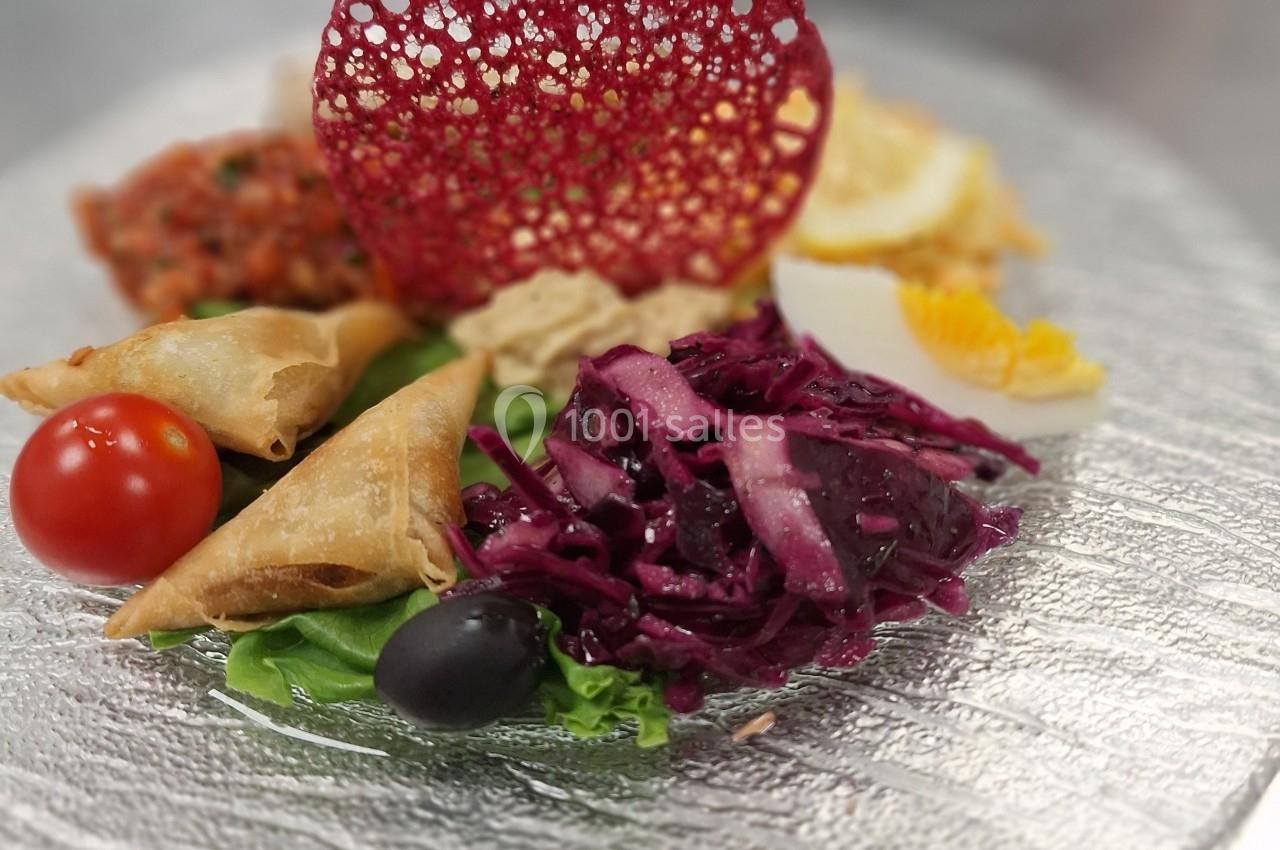 Assiette composée de samoussas, crudités, œuf dur, tomate cerise, olive noire et décoration alimentaire colorée.