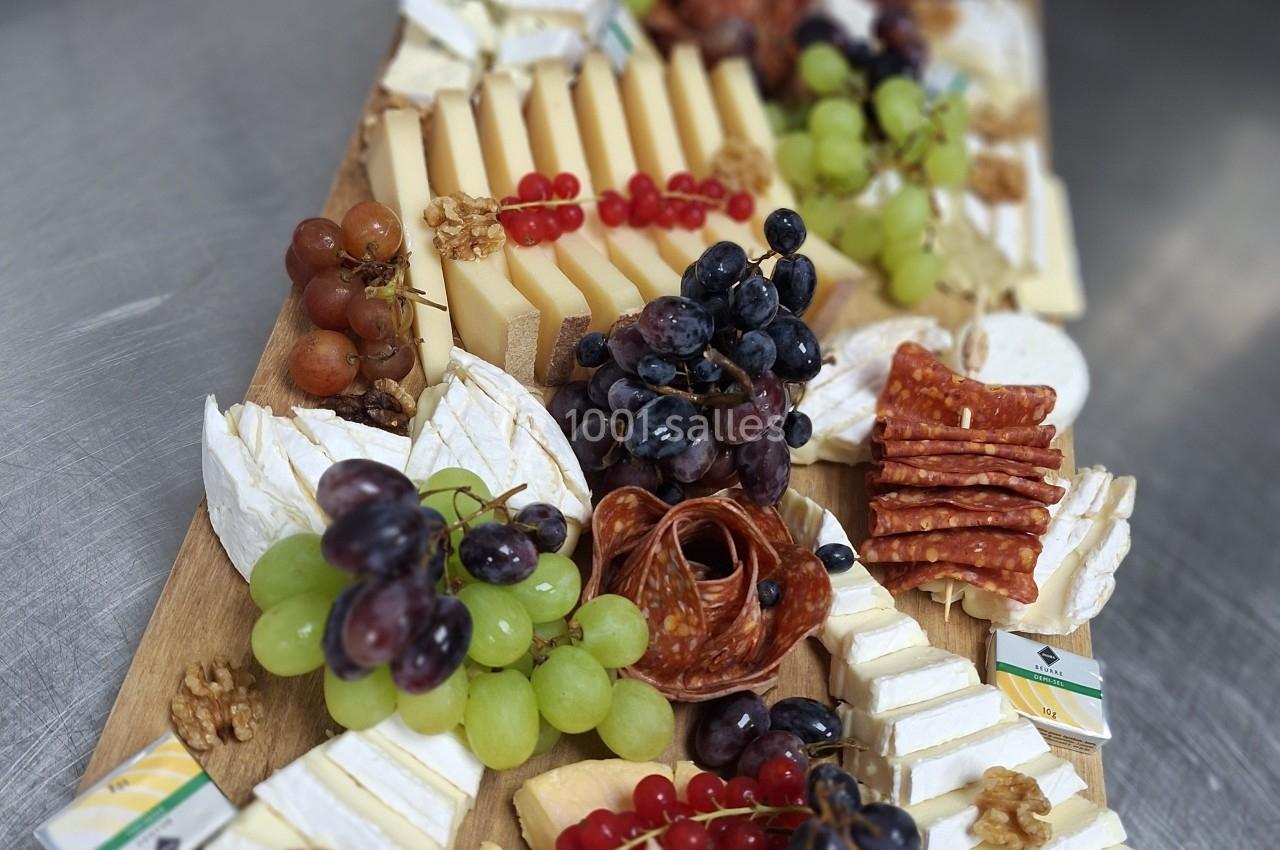 Plateau de fromages variés accompagné de fruits frais, charcuterie et noix, présenté sur une planche en bois.