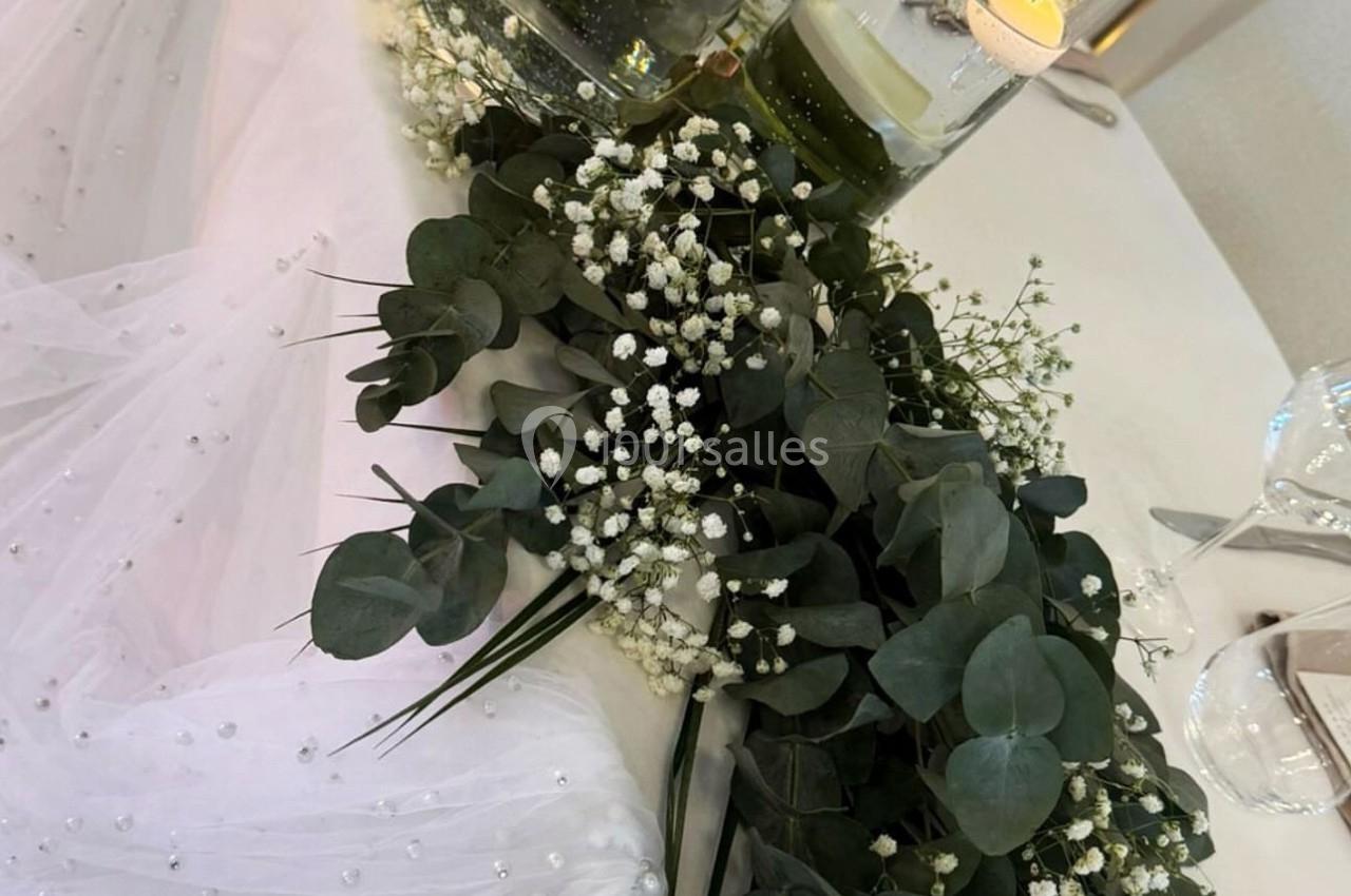 Décoration de table avec bougies flottantes, feuillage vert, gypsophile et tissu blanc perlé.
