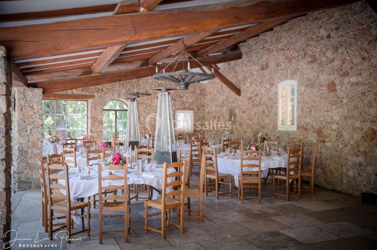 Salle de réception en pierre avec tables dressées, nappes blanches, chaises en bois et décorations florales.
