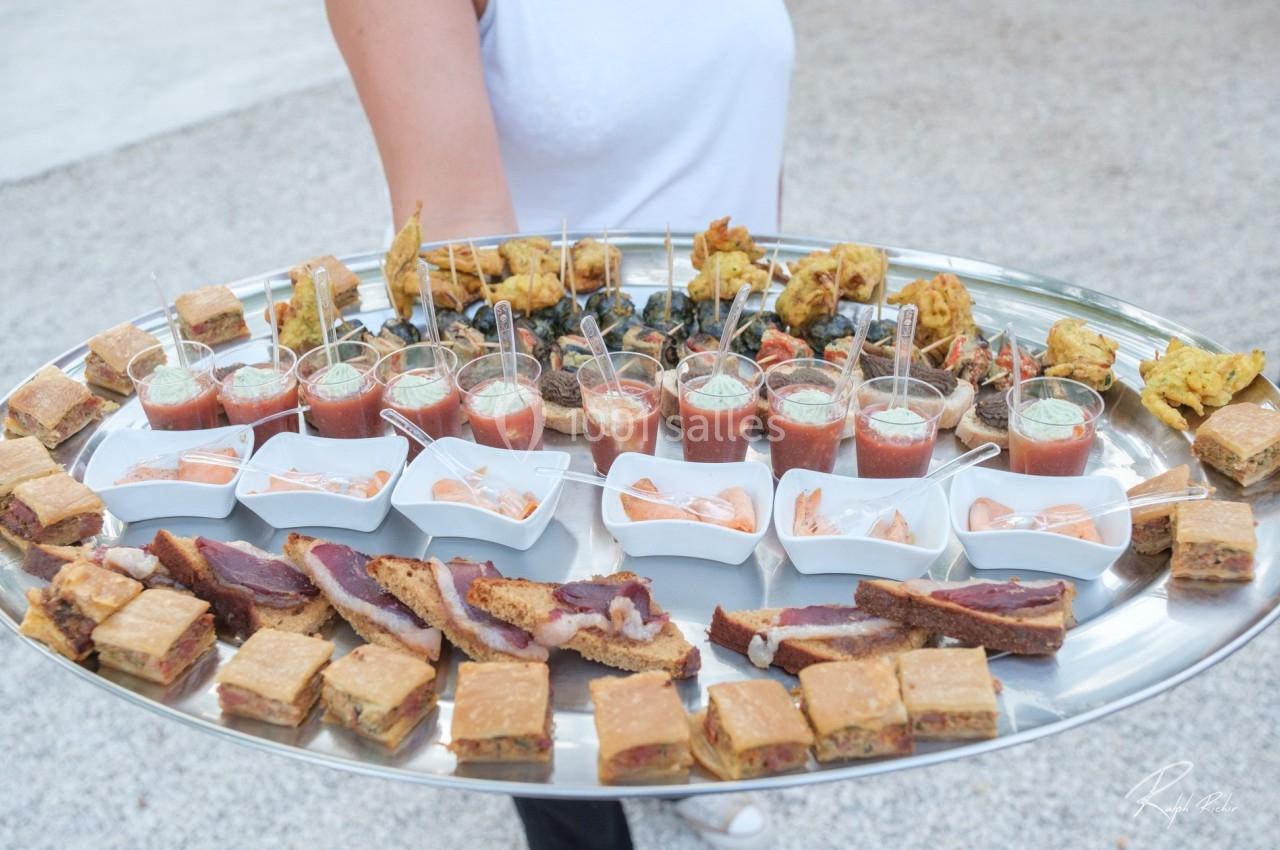 Plateau de canapés variés avec verrines, bouchées salées et amuse-bouches, tenu par une personne en extérieur.