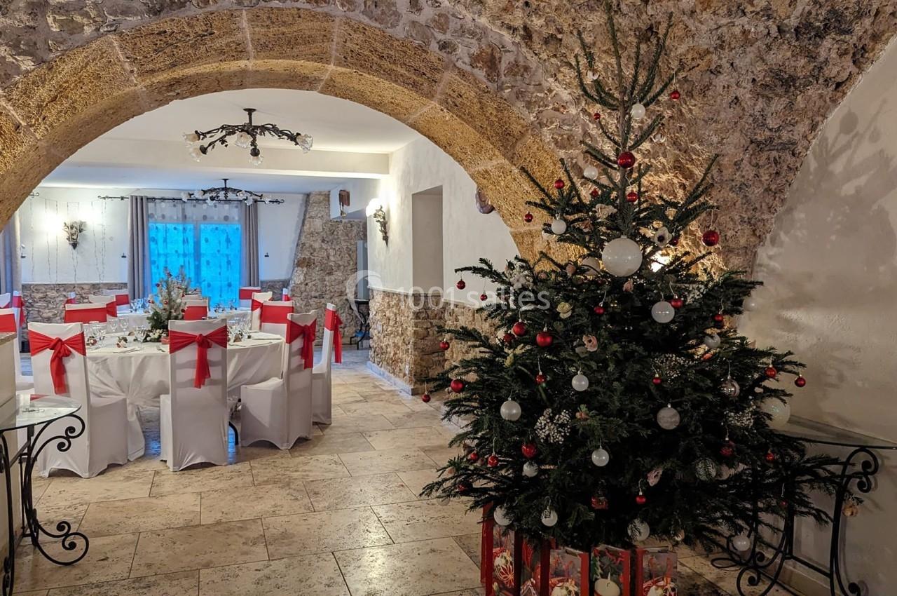 Salle décorée pour une réception avec des tables ornées de nœuds rouges et un sapin de Noël illuminé au premier plan.