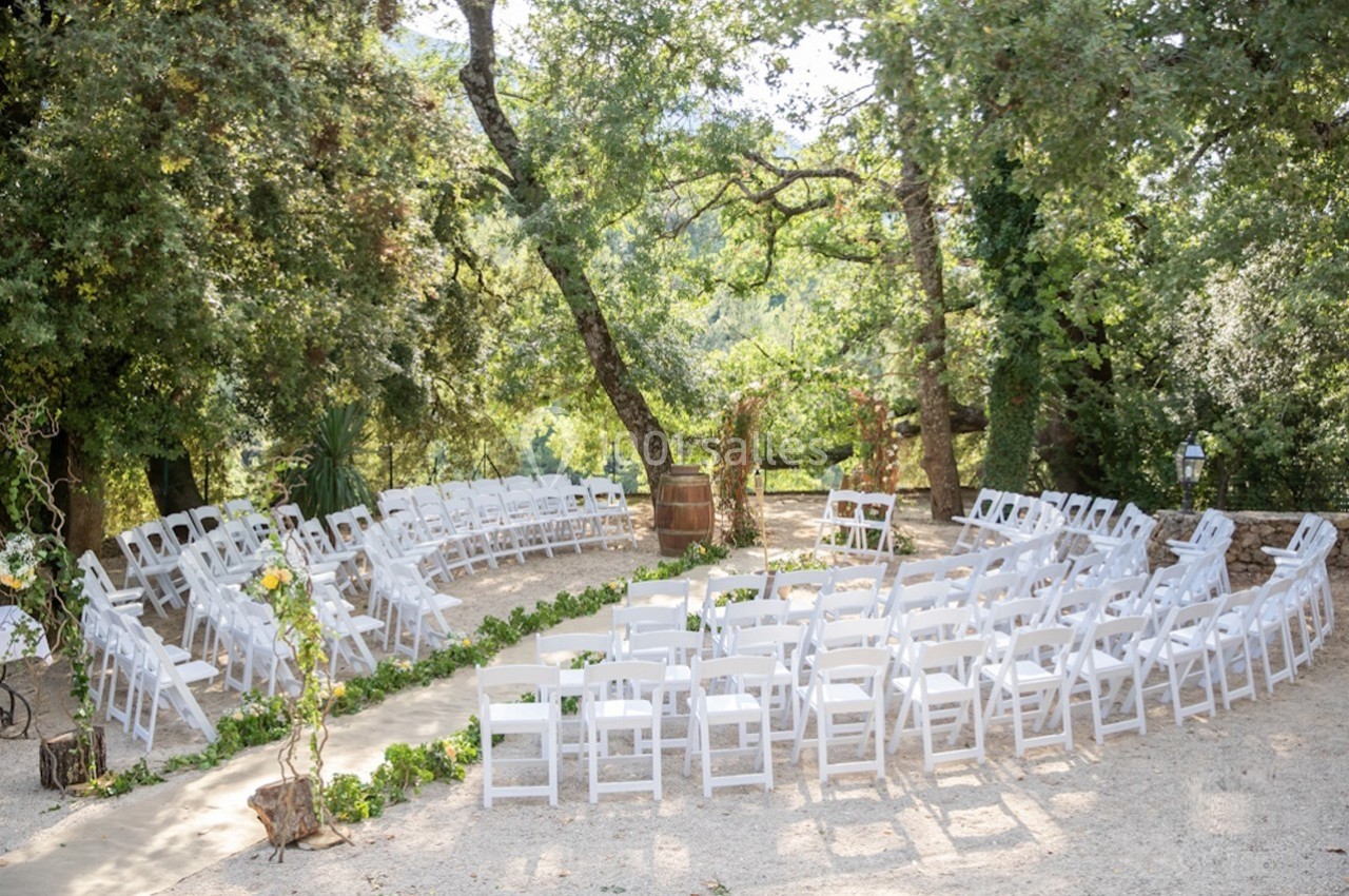 Chaises blanches disposées en cercle dans un cadre extérieur boisé, préparées pour une cérémonie en plein air.