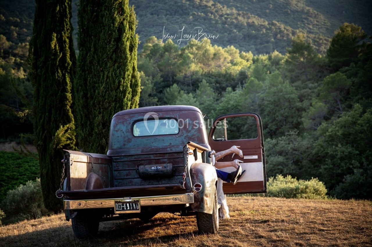 Un vieux pick-up rouillé stationné dans un paysage rural avec une personne assise sur le marchepied, porte ouverte.