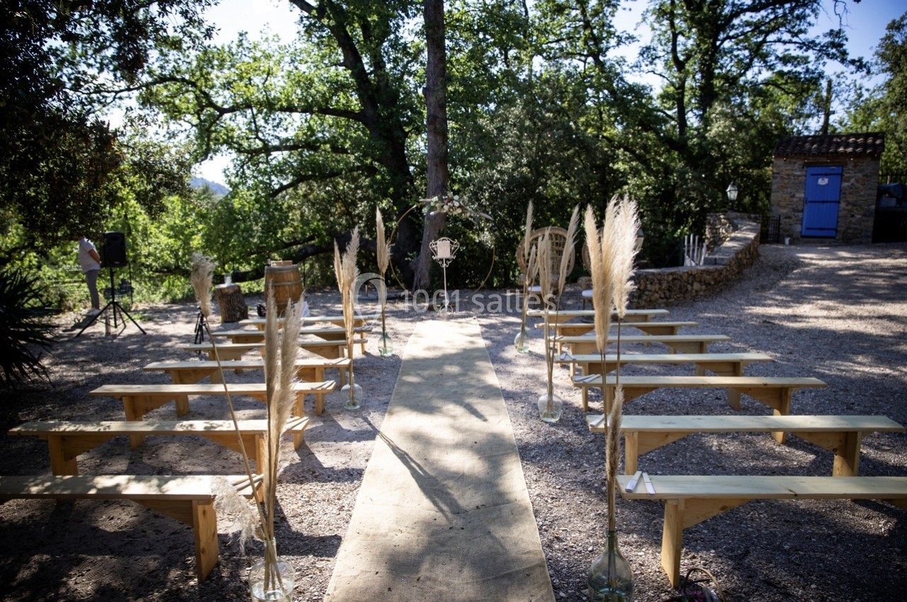 Allée centrale bordée de bancs en bois et de décorations végétales, menant à un espace de cérémonie en extérieur.
