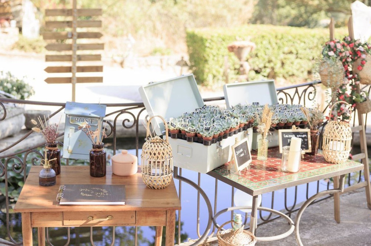 Table décorative en extérieur avec des plantes en pots, un carnet ouvert et des éléments en osier près d'un point d'eau.