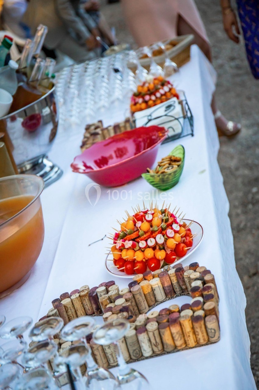 Table de buffet avec brochettes apéritives, bols de snacks, carafes de boisson et décorations en bouchons de liège.