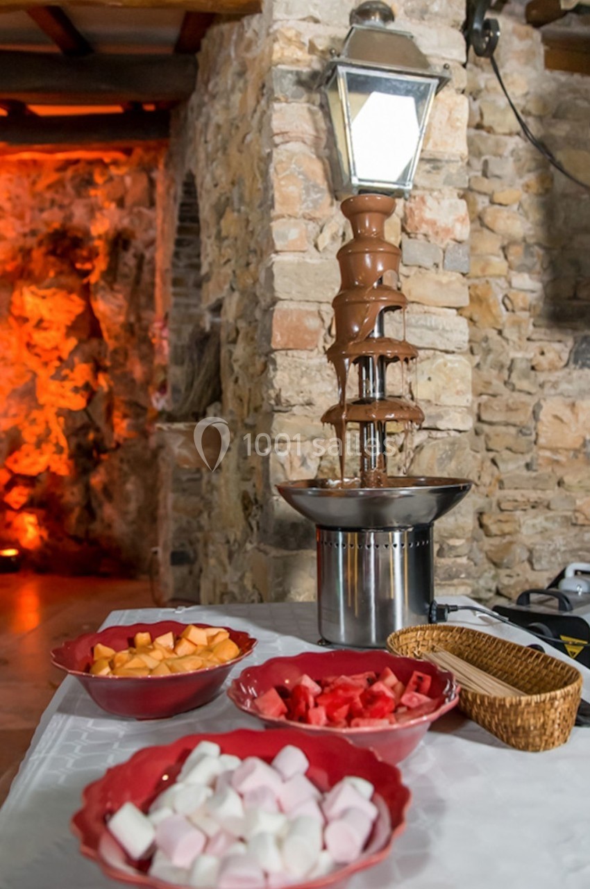 Fontaine à chocolat entourée de bols contenant des morceaux de fruits et des guimauves, disposés sur une table.
