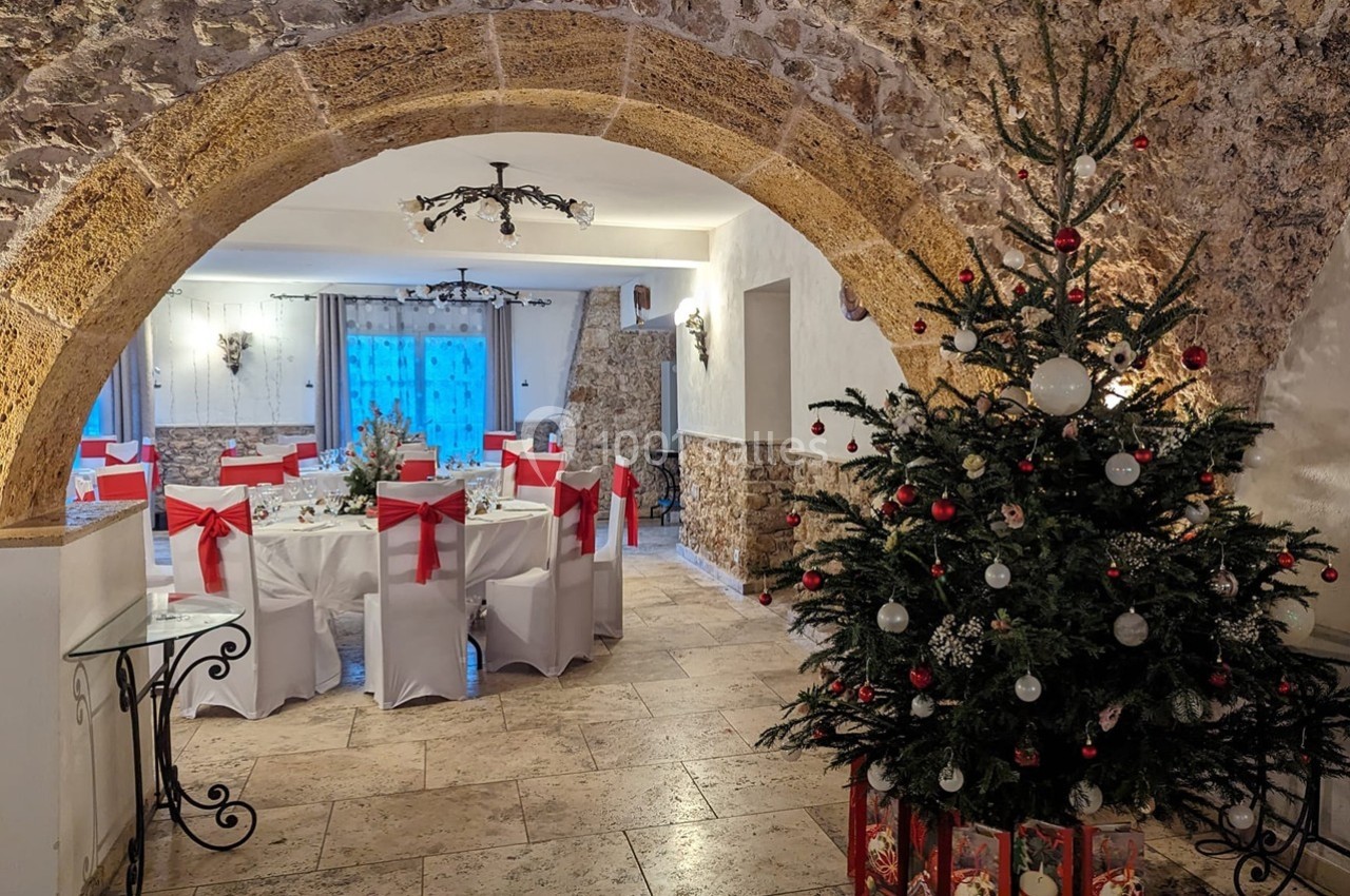 Salle voûtée décorée pour Noël avec un sapin orné de boules rouges et blanches et des tables dressées pour un repas.