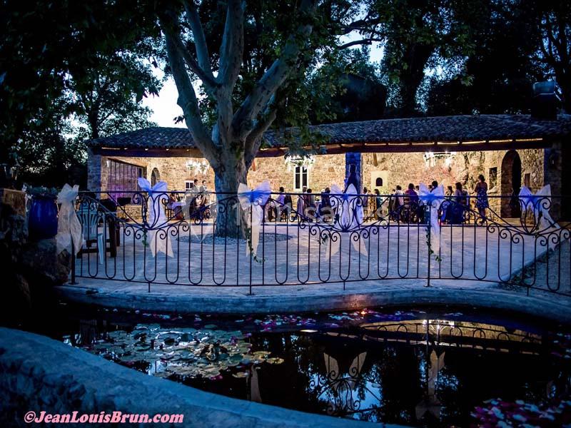 Terrasse éclairée en soirée avec des tables dressées, entourée d'arbres et d'une balustrade près d'un bassin.
