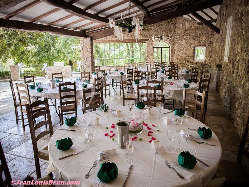 Salle de réception lumineuse avec tables rondes dressées, décorées de serviettes vertes et pétales de fleurs roses.