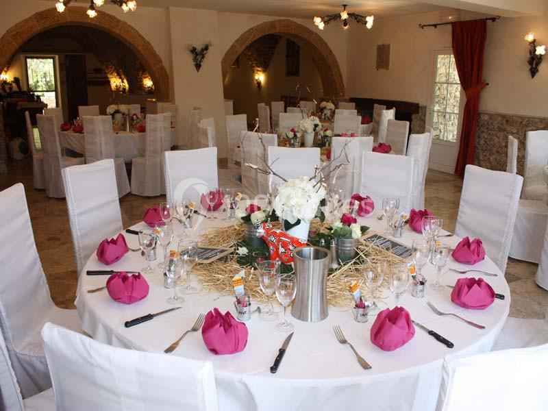 Salle de réception décorée avec des tables rondes, nappes blanches, serviettes roses pliées et centre de table floral.
