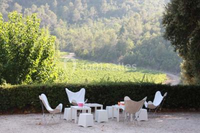 Mobilier de jardin blanc disposé sur une terrasse en gravier, avec vue sur des vignes et une forêt en arrière-plan.