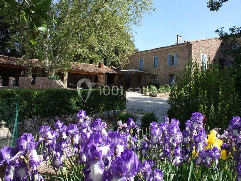 Maison en pierre entourée de verdure avec des iris violets en premier plan.