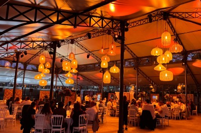 Salle de réception illuminée par des suspensions lumineuses, avec des invités assis à des tables rondes.