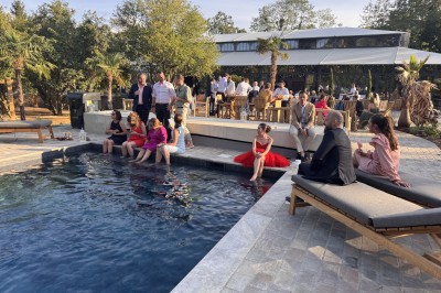 Salle de réception illuminée par des suspensions lumineuses, avec des invités assis à des tables rondes.