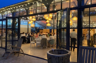 Salle de réception illuminée par des suspensions lumineuses, avec des invités assis à des tables rondes.