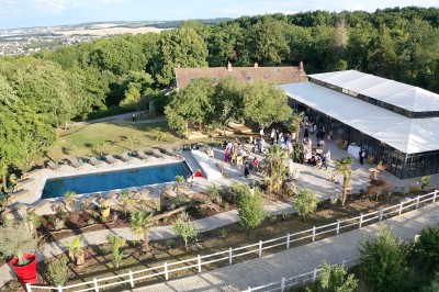 Salle de réception illuminée par des suspensions lumineuses, avec des invités assis à des tables rondes.