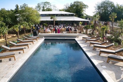 Salle de réception illuminée par des suspensions lumineuses, avec des invités assis à des tables rondes.