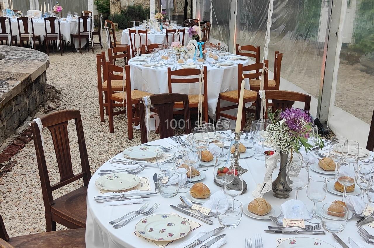 Table dressée pour un repas dans une tente transparente, avec vaisselle élégante et décorations florales.