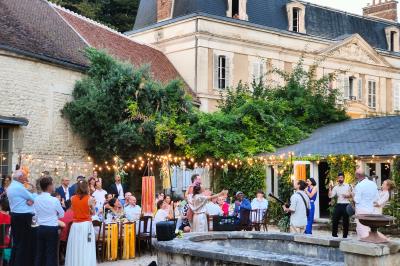 Salle lumineuse avec murs en pierre, tables en bois, poêle à bois et canapé dans un espace chaleureux.