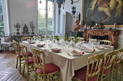 Salle lumineuse avec murs en pierre, tables en bois, poêle à bois et canapé dans un espace chaleureux.