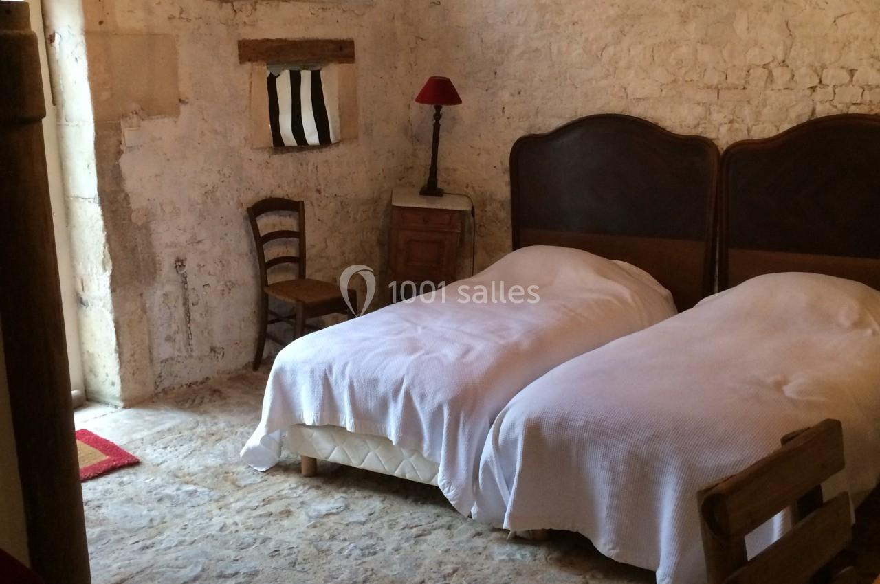 Chambre rustique avec murs en pierre, deux lits simples, un lustre, une lampe rouge et des meubles en bois.