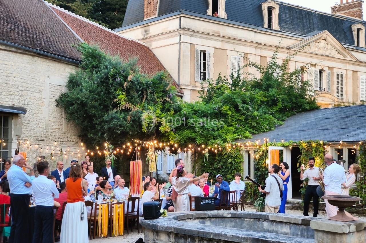 Groupe de personnes réunies dans une cour extérieure décorée de guirlandes lumineuses, près d'un bâtiment ancien.