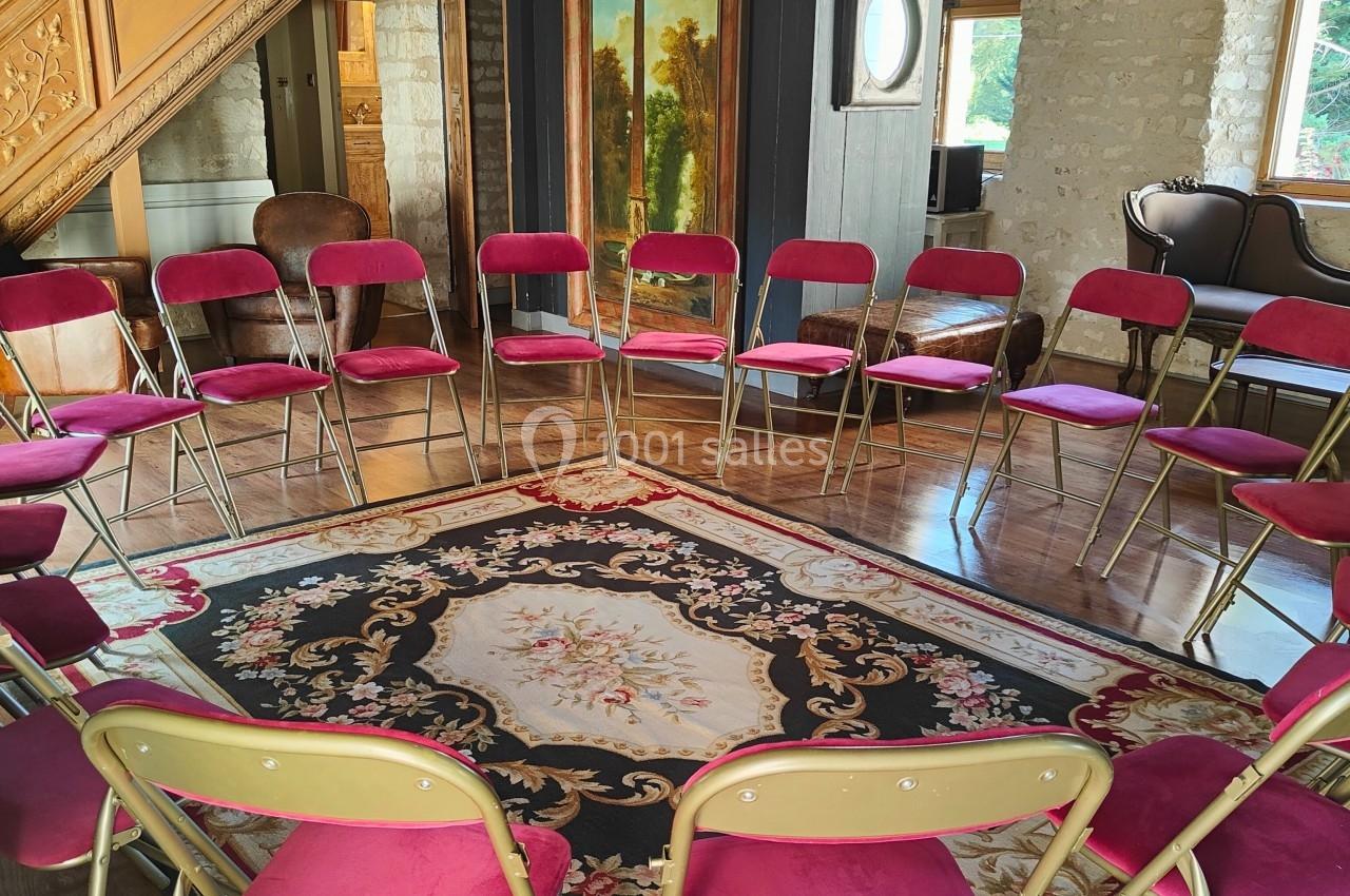 Chaises pliantes rouges disposées en cercle dans une salle rustique avec poutres apparentes et tapis décoratif au sol.