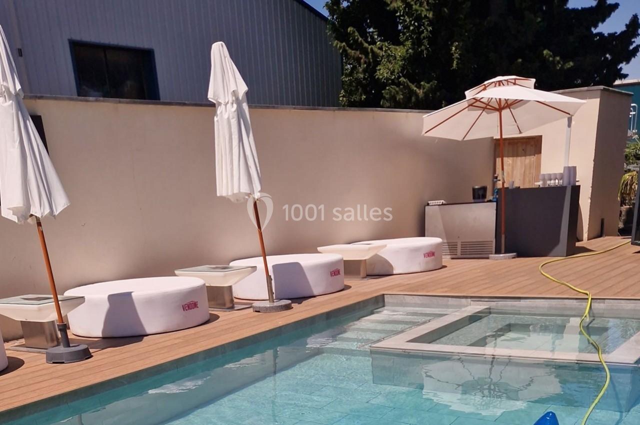 Piscine extérieure avec terrasse en bois, transats blancs, parasols et mur beige en arrière-plan.