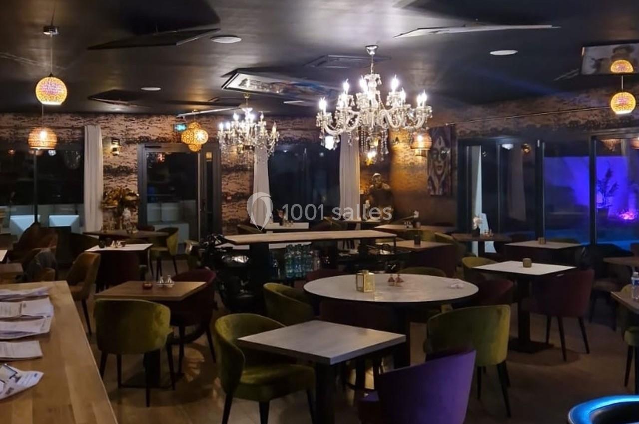 Salle de restaurant élégante avec tables en bois, chaises colorées, lustres et éclairage tamisé.