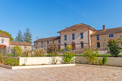 Deux chaises et une table en métal sur une terrasse pavée, près d'une pelouse et d'un bâtiment en pierre.