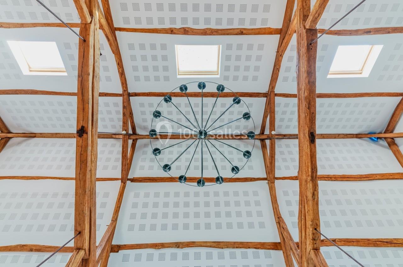 Plafond avec poutres en bois apparentes, lustre circulaire central et panneaux acoustiques blancs.