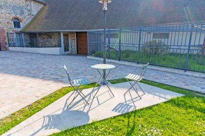 Deux chaises et une table en métal sur une terrasse pavée, près d'une pelouse et d'un bâtiment en pierre.