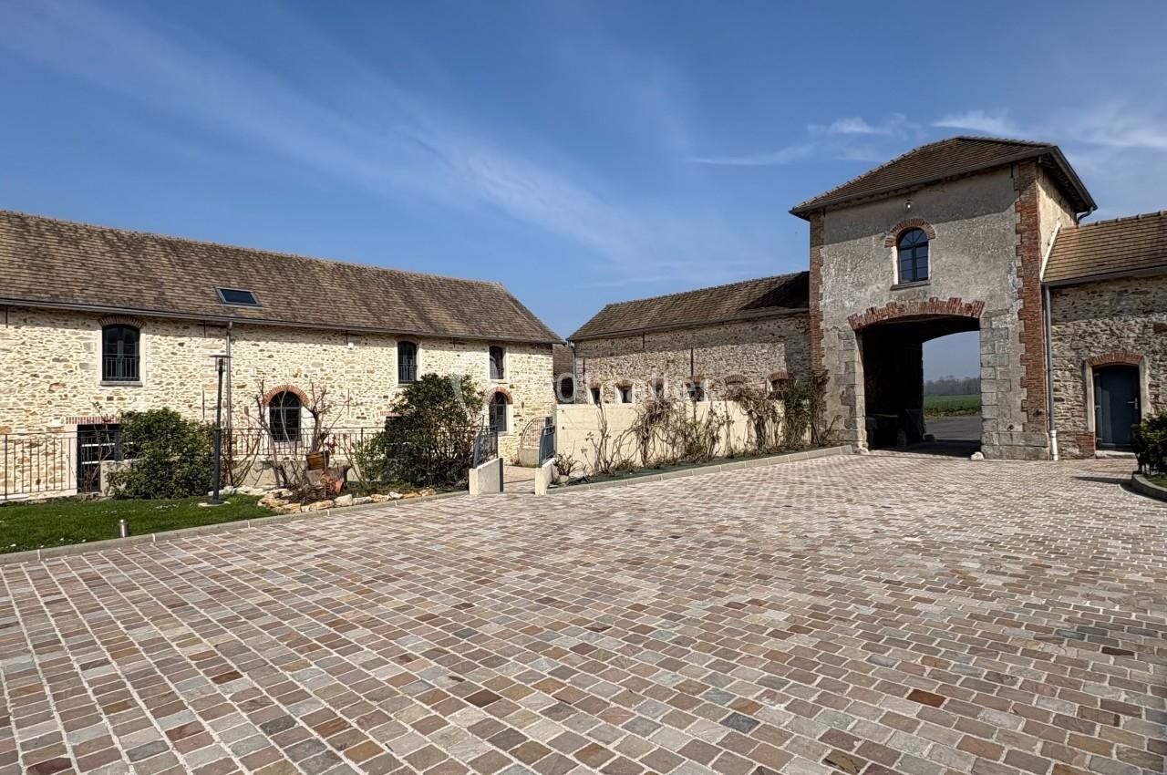 Cour pavée entourée de bâtiments en pierre et d'une grande entrée voûtée sous un ciel dégagé.