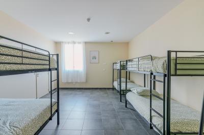 Chambre avec quatre lits superposés, draps à motifs verts, sol en carrelage gris et lumière naturelle provenant d'une…