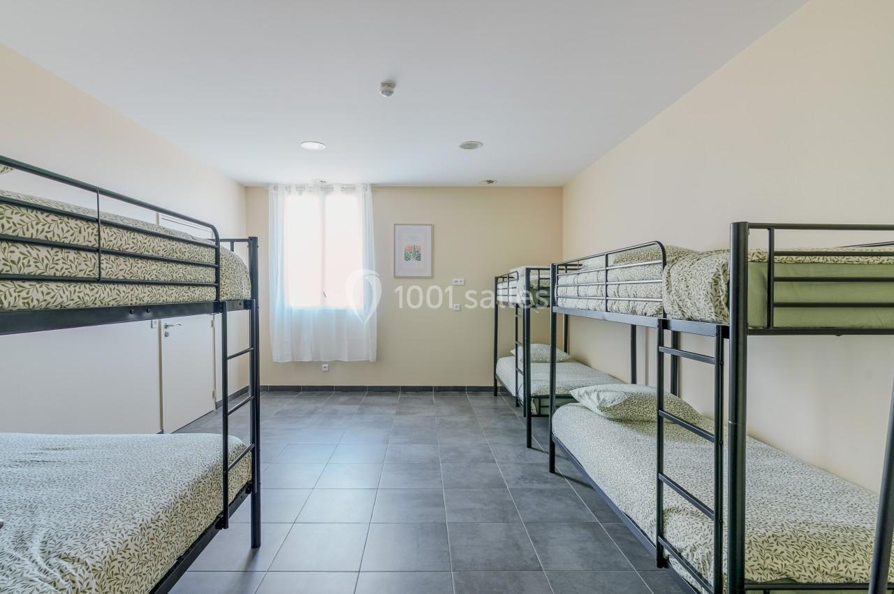 Chambre avec quatre lits superposés, draps à motifs verts, sol en carrelage gris et lumière naturelle provenant d'une…