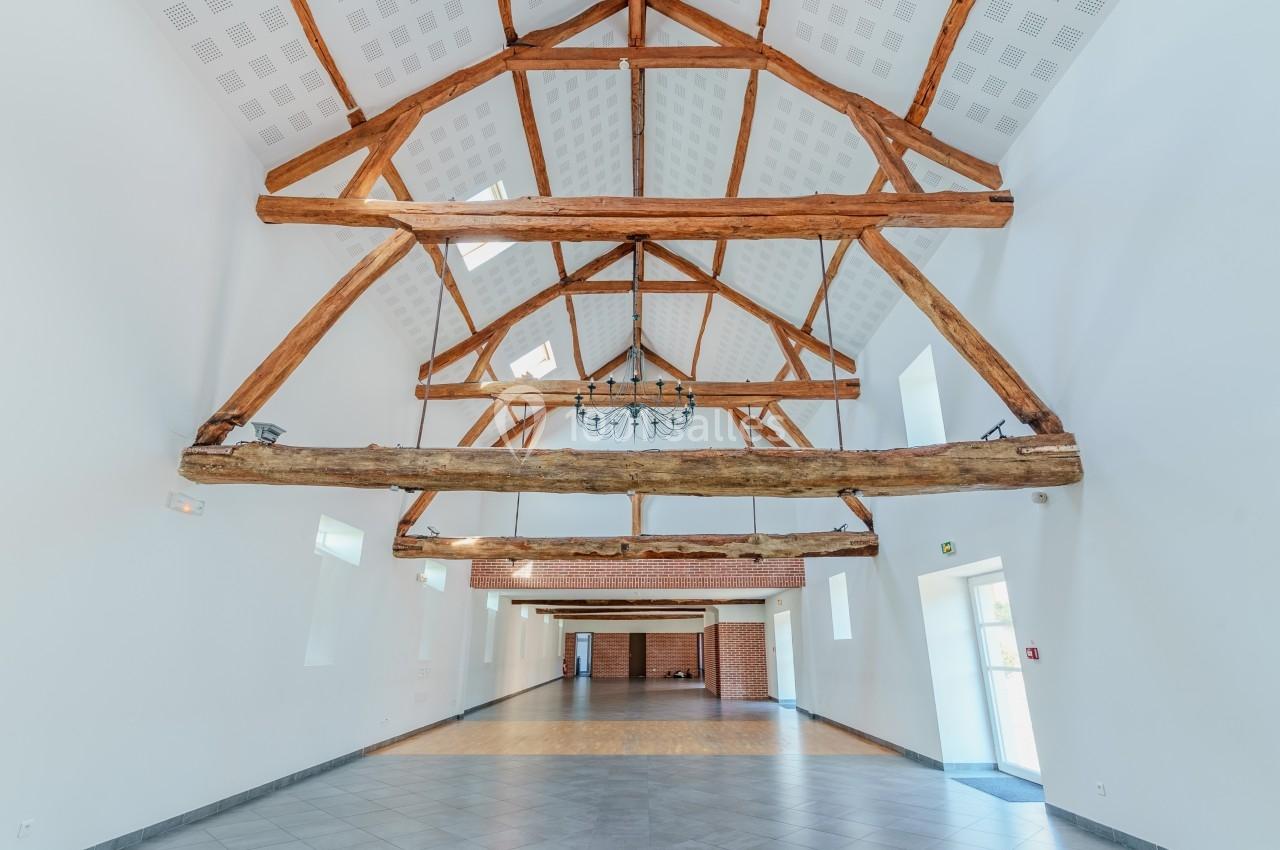 Vue intérieure d'une grande salle lumineuse avec poutres apparentes en bois et plafond haut.