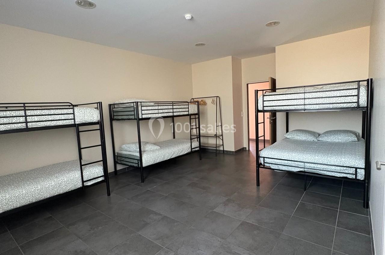 Dortoir avec lits superposés en métal, matelas blancs, sol en carrelage gris et murs clairs.